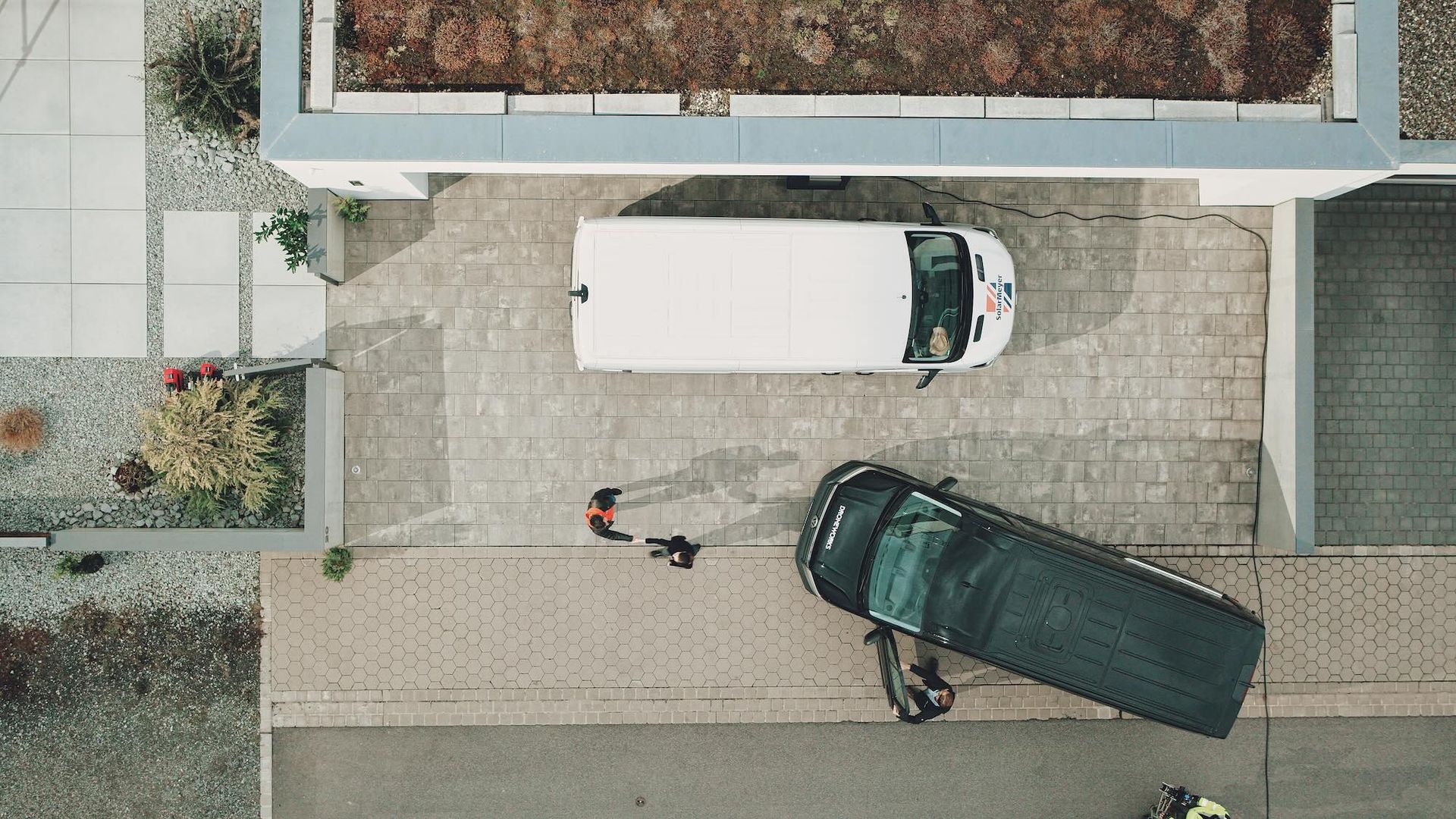 Droneworks-Einsatzfahrzeuge stehen für eine professionelle PV-Inspektion direkt vor Ort in der Einfahrt eines Kunden, fotografiert aus der Luft.